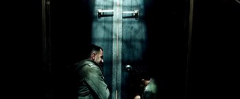 Movie still from “Three Kings” (1999), directed by David O. Russell – Two men are standing in front of a metal door; Medium shot, Overhead angle
