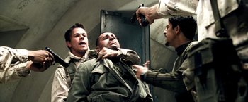 Movie still from “Three Kings” (1999), directed by David O. Russell – A group of men holding guns and a man in a green jacket; Medium shot, Over the shoulder angle