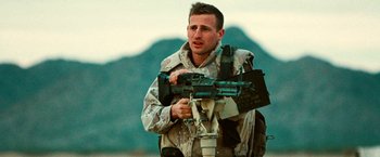 Movie still from “Three Kings” (1999), directed by David O. Russell – A man holding a gun while standing next to a mountain range; Medium shot, Low angle