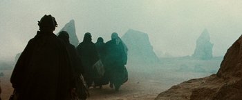 Movie still from “Three Kings” (1999), directed by David O. Russell – A group of people walking on a dirt road; Wide shot, Low angle