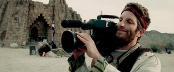 Movie still from “Three Kings” (1999), directed by David O. Russell – A man is holding a video camera in his hand; Close Up shot, Low angle