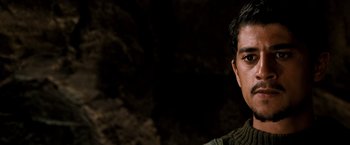 Movie still from “Three Kings” (1999), directed by David O. Russell – A young man is posing for a picture in front of a cave; Close Up shot, High angle