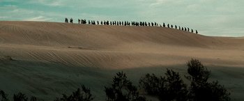 Movie still from “Three Kings” (1999), directed by David O. Russell – A large group of people walking up a sand dune; Extreme Wide shot, High angle