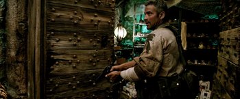 Movie still from “Three Kings” (1999), directed by David O. Russell – A man holding a gun standing in front of a wall; Medium shot, Over the shoulder angle
