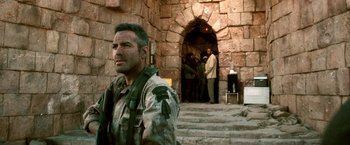 Movie still from “Three Kings” (1999), directed by David O. Russell – A man standing in front of a stone wall; Medium shot, Over the shoulder angle