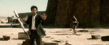 Movie still from “Three Kings” (1999), directed by David O. Russell – A man in a suit and tie standing in the sand; Wide shot, Over the shoulder angle