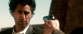 Movie still from “Three Kings” (1999), directed by David O. Russell – A man in a suit and tie holding a gun; Close Up shot, Over the shoulder angle
