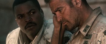 Movie still from “Three Kings” (1999), directed by David O. Russell – A man in fatigues is looking at the camera while another man looks on; Close Up shot, Low angle