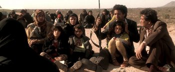Movie still from “Three Kings” (1999), directed by David O. Russell – A group of people sitting on the ground in the desert; Medium shot, Low angle