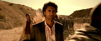 Movie still from “Three Kings” (1999), directed by David O. Russell – A man in a suit and tie standing in front of a group of people; Close Up shot, Over the shoulder angle