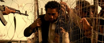 Movie still from “Three Kings” (1999), directed by David O. Russell – A man in a suit and tie standing next to barbed wire; Medium shot, Low angle