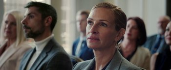 Movie still from “Ticket to Paradise” (2022), directed by Ol Parker – A person sitting in a room with other people; Close Up shot, Over the shoulder angle