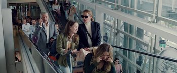 Movie still from “Ticket to Paradise” (2022), directed by Ol Parker – A group of people riding up an escalator in an airport; Medium shot, Over the shoulder angle