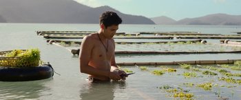 Movie still from “Ticket to Paradise” (2022), directed by Ol Parker – A man in the water looking at his cell phone; Medium shot, High angle