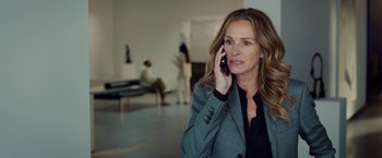 Movie still from “Ticket to Paradise” (2022), directed by Ol Parker – A woman talking on a cell phone while sitting in a room; Medium shot, Over the shoulder angle