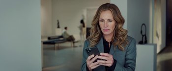 Movie still from “Ticket to Paradise” (2022), directed by Ol Parker – A woman holding a cell phone while standing in a room; Close Up shot, Low angle