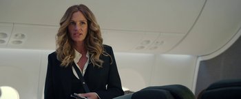 Movie still from “Ticket to Paradise” (2022), directed by Ol Parker – A woman in a black suit is holding a cell phone; Medium shot, Over the shoulder angle