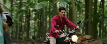 Movie still from “Ticket to Paradise” (2022), directed by Ol Parker – A man riding on the back of a motorcycle in the woods; Medium shot, High angle