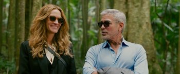 Movie still from “Ticket to Paradise” (2022), directed by Ol Parker – A man and a woman wearing sunglasses in the woods; Medium shot, Over the shoulder angle