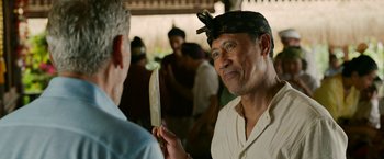 Movie still from “Ticket to Paradise” (2022), directed by Ol Parker – A man holding a knife in front of another man in front of a crowd; Close Up shot, Over the shoulder angle