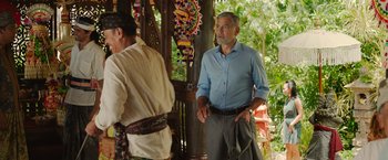 Movie still from “Ticket to Paradise” (2022), directed by Ol Parker – A man standing next to another man wearing a blue shirt; Medium shot, Over the shoulder angle