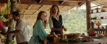 Movie still from “Ticket to Paradise” (2022), directed by Ol Parker – Two women standing next to each other in front of a table; Medium shot, Over the shoulder angle