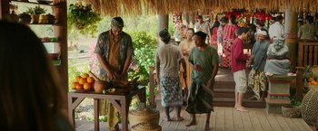 Movie still from “Ticket to Paradise” (2022), directed by Ol Parker – A group of people standing around a building with food; Wide shot, Over the shoulder angle