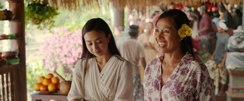 Movie still from “Ticket to Paradise” (2022), directed by Ol Parker – Two women are standing together and smiling for the camera; Medium shot, Over the shoulder angle