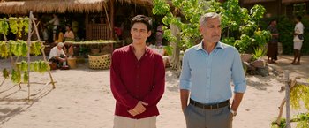 Movie still from “Ticket to Paradise” (2022), directed by Ol Parker – A man standing next to another man on a beach; Medium shot, Over the shoulder angle