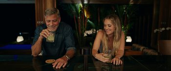 Movie still from “Ticket to Paradise” (2022), directed by Ol Parker – A man and a woman sitting at a table with drinks; Medium shot, Over the shoulder angle