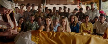 Movie still from “Ticket to Paradise” (2022), directed by Ol Parker – A group of people sitting in front of each other in a room; Medium shot, Over the shoulder angle