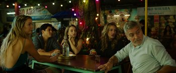 Movie still from “Ticket to Paradise” (2022), directed by Ol Parker – A group of people sitting at a table in a bar; Medium shot, Over the shoulder angle