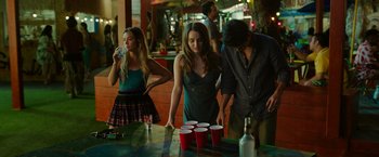 Movie still from “Ticket to Paradise” (2022), directed by Ol Parker – A group of young people standing around a table with cups; Medium shot, Over the shoulder angle