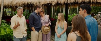 Movie still from “Ticket to Paradise” (2022), directed by Ol Parker – Two women and a man standing next to each other in front of a thatched hut; Wide shot, Over the shoulder angle
