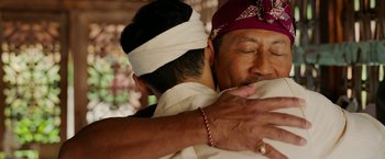 Movie still from “Ticket to Paradise” (2022), directed by Ol Parker – A man hugging another man with a white bandanna on his head; Close Up shot, Over the shoulder angle