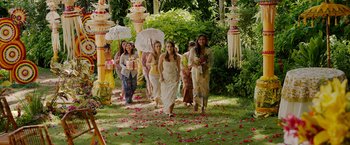 Movie still from “Ticket to Paradise” (2022), directed by Ol Parker – A group of people walking down a path holding umbrellas; Extreme Wide shot, High angle