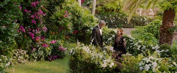 Movie still from “Ticket to Paradise” (2022), directed by Ol Parker – A man and a woman standing next to a flower garden; Wide shot, High angle