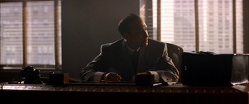 Movie still from “Timecop” (1994), directed by Peter Hyams – A man sitting at a desk in a suit and tie; Medium shot, Low angle