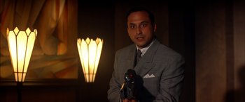 Movie still from “Timecop” (1994), directed by Peter Hyams – A man in a gray suit holding a camera in front of a lamp; Close Up shot, Low angle