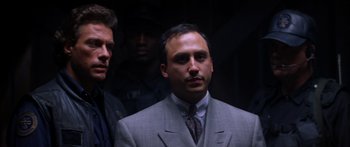 Movie still from “Timecop” (1994), directed by Peter Hyams – A man in a suit and tie standing next to another man; Close Up shot, Low angle