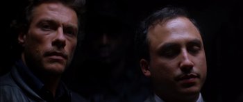 Movie still from “Timecop” (1994), directed by Peter Hyams – Two men in a dark room looking at the camera; Close Up shot, Over the shoulder angle