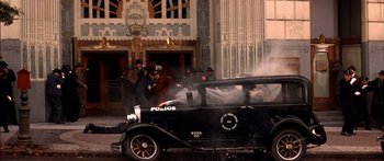 Movie still from “Timecop” (1994), directed by Peter Hyams – An old police car is parked in front of a building; Wide shot, Low angle