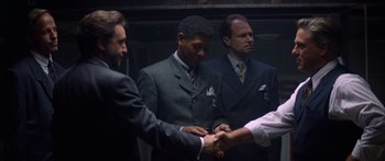 Movie still from “Timecop” (1994), directed by Peter Hyams – A group of men in suits shaking hands in a room; Medium shot, Over the shoulder angle