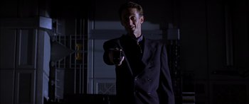 Movie still from “Timecop” (1994), directed by Peter Hyams – A man in a black suit holding a glass of wine; Medium shot, Low angle