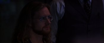Movie still from “Timecop” (1994), directed by Peter Hyams – A man with long hair and glasses is looking at the camera; Close Up shot, Over the shoulder angle