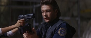 Movie still from “Timecop” (1994), directed by Peter Hyams – A man holding a gun while wearing a police uniform; Close Up shot, Low angle