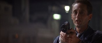 Movie still from “Timecop” (1994), directed by Peter Hyams – A man in a suit and tie holding a gun in his hand; Close Up shot, Low angle
