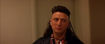 Movie still from “Timecop” (1994), directed by Peter Hyams – A man with long black hair and a long mohawk; Close Up shot, Over the shoulder angle
