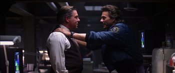 Movie still from “Timecop” (1994), directed by Peter Hyams – Two men in a room one has his arm around the shoulder of another man; Medium shot, Over the shoulder angle