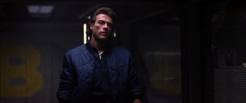 Movie still from “Timecop” (1994), directed by Peter Hyams – A man wearing a blue jacket standing in a dark room; Medium shot, Low angle